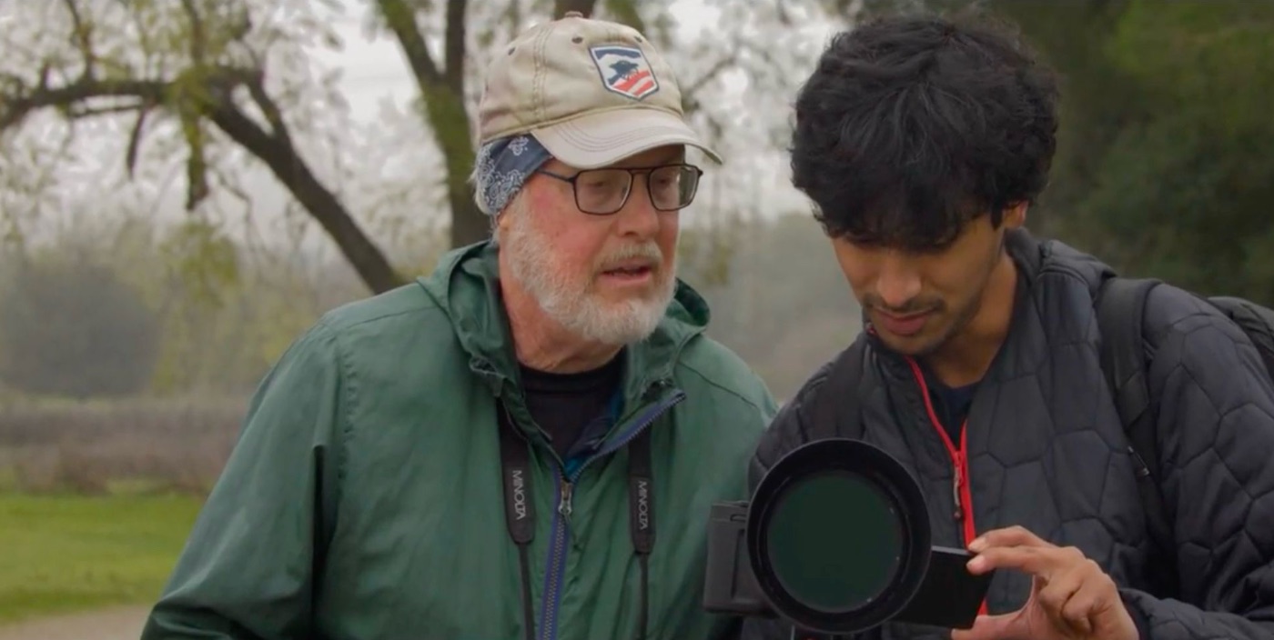 Two people look at the screen of a camera together in a park